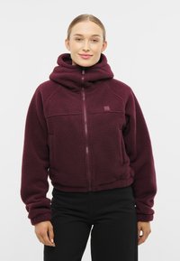 Burgundy fleece vetoketjullinen takki korkealla kauluksella, etutaskuilla ja ribbausnäteillä hihoilla. Pehmeä rakenne ja rento istuvuus.