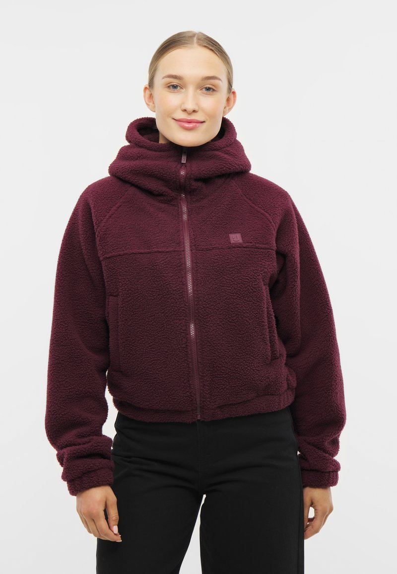 Burgundy fleece vetoketjullinen takki korkealla kauluksella, etutaskuilla ja ribbausnäteillä hihoilla. Pehmeä rakenne ja rento istuvuus.