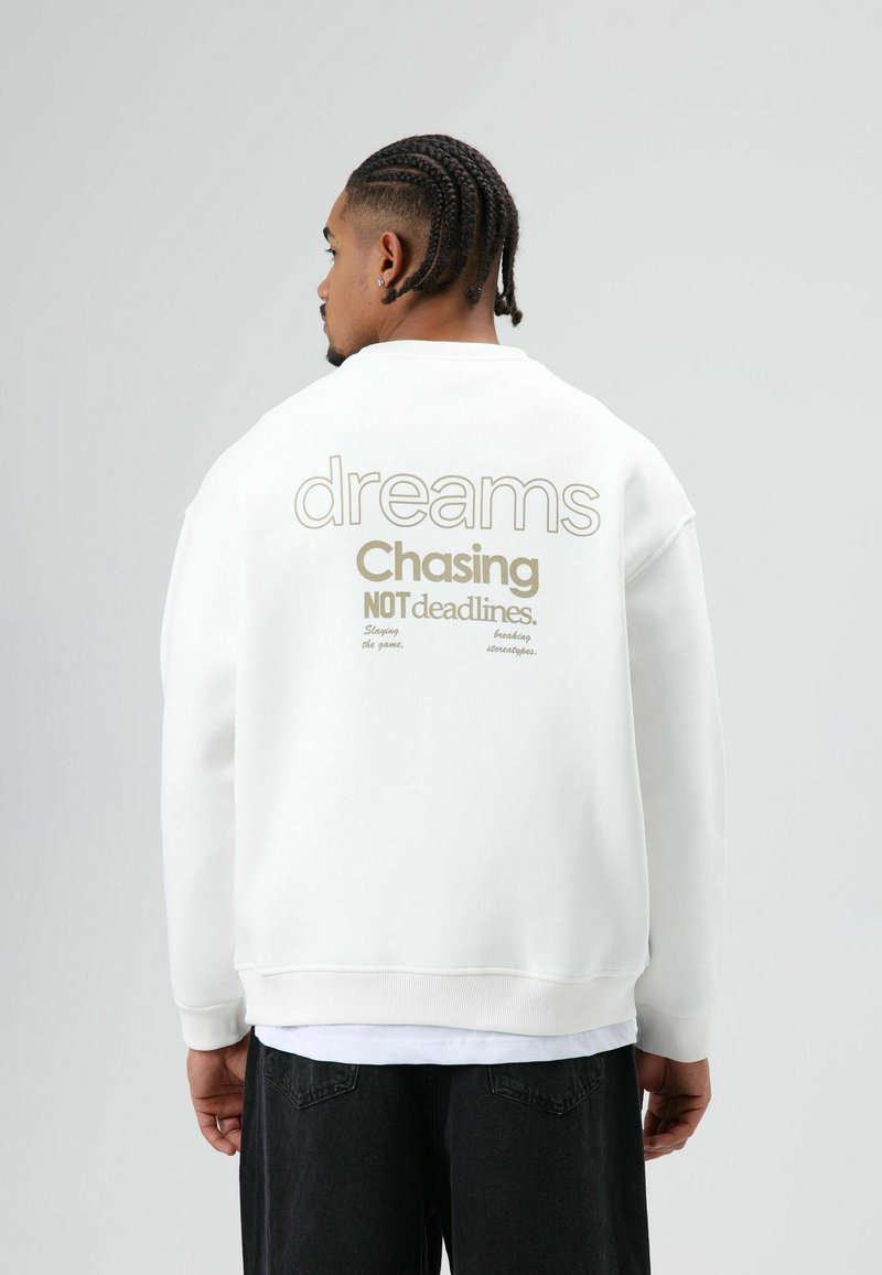 Witte sweatshirts met opvallende tekst op de achterkant: "dromen najagen, geen deadlines." Casual design met een ontspannen pasvorm en geribbelde manchetten.