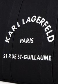 Czarna tkanina o fakturze z wyraźnym białym napisem: "KARL LAGERFELD PARIS 21 RUE ST-GUILAUME" ułożonym w łuk.