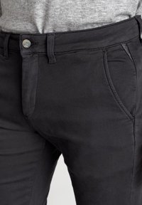 Pantaloni neri attillati realizzati in tessuto leggero con chiusura a bottone e cerniera, dotati di tasche frontali e dettagli di cucitura eleganti.