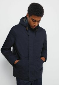 Giacca con cappuccio blu navy, con chiusura a bottoni, grandi tasche e cordini regolabili. Texture liscia e design casual.