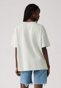 Lys grøn oversized t-shirt med korte ærmer, rund halsudskæring og blød, glat tekstur, parret med denimshorts med frynset kant.