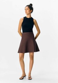 Jupe évasée marron avec une texture lisse, assortie à un haut moulant sans manches noir. La mannequin porte des sandales à talons noires.