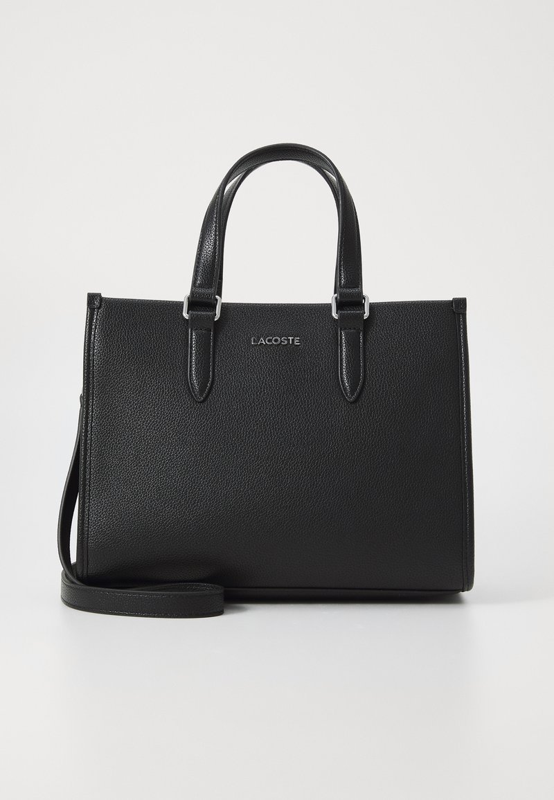Sac à main en cuir noir avec une finition texturée, deux poignées supérieures, une bandoulière réglable et des accessoires en métal argenté. Logo Lacoste centré.