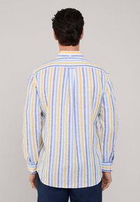 Camisa ligera de botones con rayas verticales en amarillo, azul y blanco. Ajuste entallado, con mangas largas y un dobladillo redondeado.