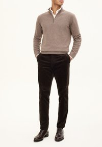 Maglione marrone con collo a zip, camicia bianca con colletto, pantaloni in velluto a coste scuri e scarpe in pelle marrone. Concentrati sulle trame e sul contrasto di colori.