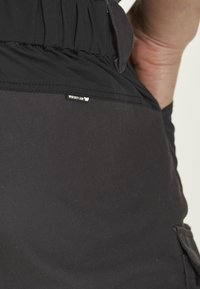 Svarta tygbyxor med en texturerad yta, med en rynkad midja och en liten "Whistler"-etikett nära fickan.