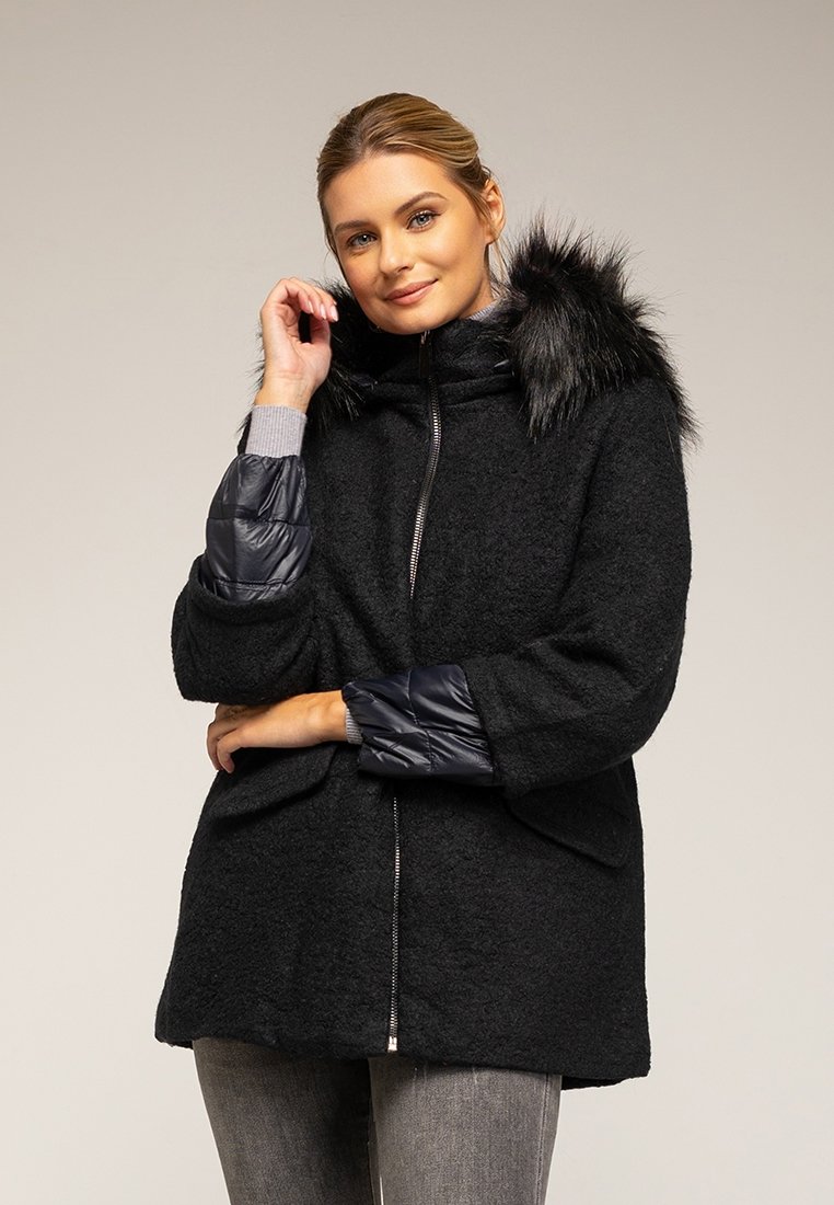 Czarny płaszcz o teksturowanej wełnianej powierzchni, z kapturem z sztucznego futra i błyszczącymi granatowymi rękawami. Ma przednie kieszenie i zamek błyskawiczny.