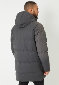 Giacca imbottita grigia con cappuccio, caratterizzata da un design trapuntato, tasche laterali e una texture liscia; taglio alla vita con vestibilità leggermente sagomata.