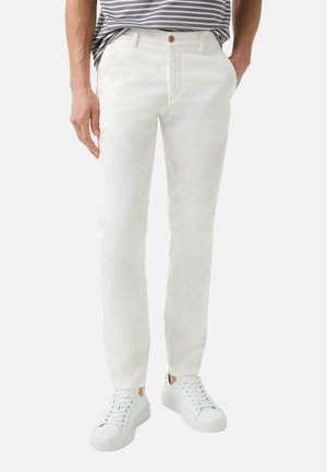 Witte katoenen broek met een rechte snit, voordeelpockets en een knoopsluiting, gecombineerd met witte sneakers. Bovenaan een horizontaal gestreepte shirt.