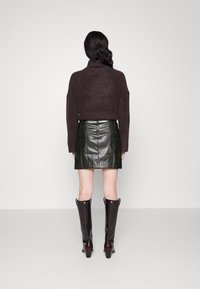 Brun cropped genser, grønn lær mini skjørt, og svarte knehøye støvler med hæl. Glatte teksturer og definerte linjer gjennom hele antrekket.
