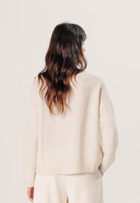 Helle beige, strukturierte Pullover mit lockerer Passform, langen Ärmeln und geripptem Saum, der ein dezentes Wellenmuster aufweist.