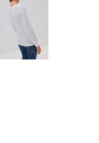 White long-sleeve top made from a soft, light material, featuring a round neckline and a slim fit, paired with blue denim jeans.