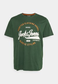 Grønn bomull t-skjorte med rund hals, med et hvitt og oransje grafisk trykk: "Jack & Jones" og "craftede klær" i retro font.