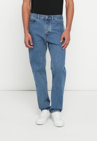 Vaqueros de denim azul claro con un diseño de pierna recta, cinco bolsillos y cierre de botón. Combinados con una camiseta negra y zapatillas blancas.