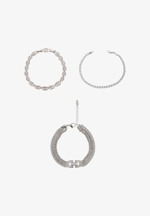 Trois bracelets en argent sont exposés : un style chaîne à maillons, une chaîne délicate à billes, et une large chaîne plate texturée avec un fermoir décoratif.