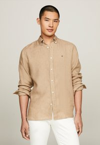 Camicia beige con bottoni realizzata in tessuto texturizzato, con colletto e maniche arrotolate, e un piccolo logo sul petto.