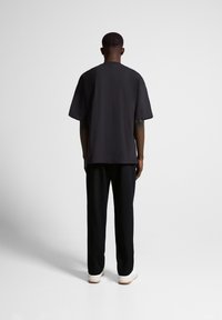 Camiseta de algodón negra de estilo oversize con mangas cortas, escote redondo y corte recto, combinada con pantalones negros y zapatillas blancas.