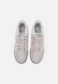 Světlé šedé tenisky Nike Air Force 1 s vrškem z textilní síťoviny a semiše, kulatou špičkou, plochými tkaničkami, polstrovaným lemem a černou gumovou podrážkou.
