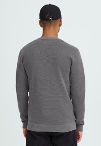 Pulover gri tricotat, cu guler rotund, manșete și tiv rib, material texturat, croială mulată, vedere din spate, purtat cu pantaloni negri și șapcă.