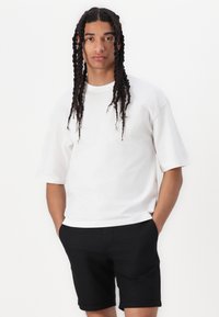 White cotton t-shirt with short sleeves, crew neckline, and relaxed fit. Paired with black shorts, fabric is smooth without patterns.