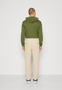 Olivengrønn hettegenser med baklomme, kombinert med lysebeige cargo-bukser som har sidelommer og rett ben-design.