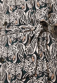 Robe à motifs présentant une impression audacieuse de tigres en noir, blanc et beige sur un fond vert foncé, avec des boutons et une taille nouée.