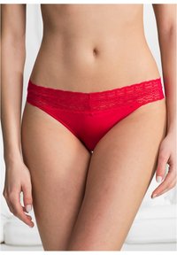 Mutandine rosse con bordi in pizzo, realizzate in un tessuto liscio. La vita presenta un bordo in pizzo decorativo e una forma aderente.