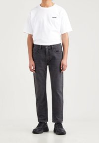 Camiseta de algodón blanca con el logo negro de Levi's, combinada con jeans de denim negros de corte recto y con bolsillos delanteros. Zapatillas negras completan el look.