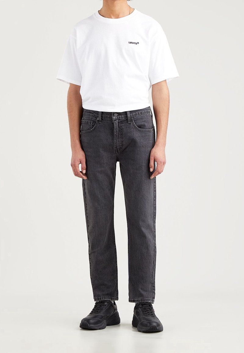Camiseta de algodón blanca con el logo negro de Levi's, combinada con jeans de denim negros de corte recto y con bolsillos delanteros. Zapatillas negras completan el look.