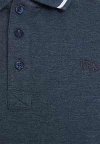 Polo de color azul marino con un tejido texturizado, cuatro botones oscuros y una franja blanca de acento en el cuello. Detalle bordado "CRS".