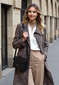 Cappotto a scacchi marrone, dolcevita crema, camicia bianca con bottoni, pantaloni beige. Borsa a tracolla nera con pattina e dettaglio anello in argento.