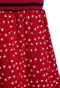 Robe fleurie rouge avec taille élastique, arborant des motifs de fleurs blanches et des accents bleus. Le tissu semble doux et texturé avec un design froncé.