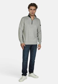 Grijze zip-up sweatshirt met zwarte kraag, gedragen met donkere jeans en witte sneakers. Heeft lange mouwen en geribde manchetten. Minimalistisch ontwerp.