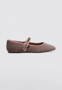 Zapato plano de ante marrón con punta afilada, ribete rosa y una correa decorativa en el tobillo con un hebilla circular. Suela de goma.