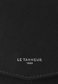 Pelle nera texturizzata con logo in bianco "LE TANNEUR 1898" in rilievo. Presenta linee pulite e cuciture visibili lungo i bordi.