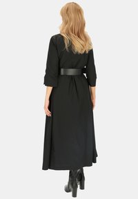 Czarna długa sukienka z rękawami o długości trzy czwarte i paskiem w talii. Posiada zwiewny krój oraz gładki, lekki materiał.