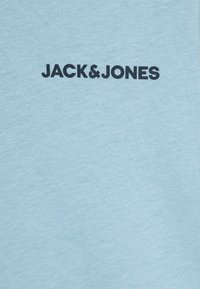 Világoskék pamut póló, a "JACK&JONES" logóval, vastag fekete betűkkel. Simas ágú textúra, letisztult dizájn, rövid ujjú.