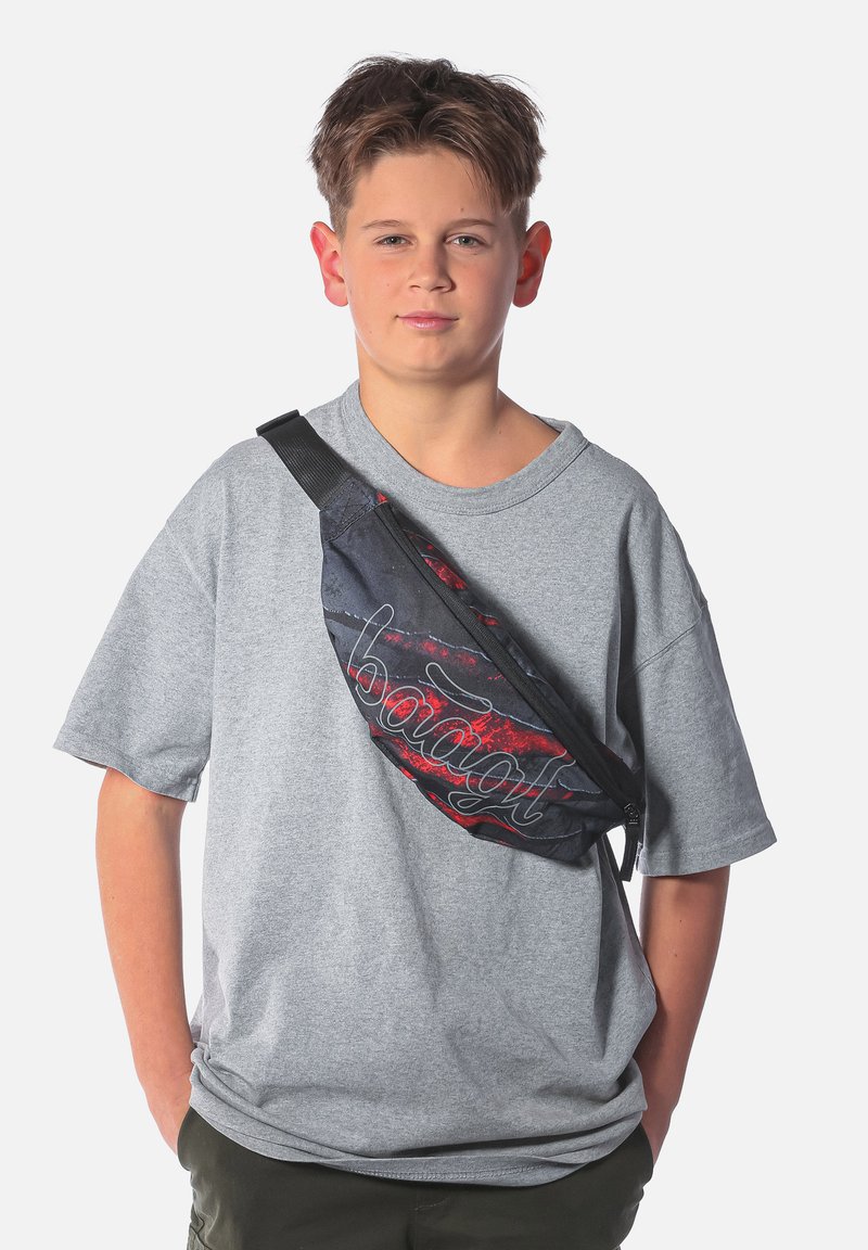 Maglietta a maniche corte grigia, borsa in vita nera e rossa con zip. La borsa è caratterizzata da un logo bianco stilizzato e una superficie in tessuto testurizzato.