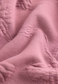 Tekstureret lyserødt stof med et forhøjet mønster af blomster motiver. Væven er blød og tekstureret, hvilket giver en taktil kvalitet.