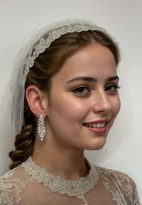 Chandelier earrings with silver tones, featuring clear gemstones and ornate floral patterns. Model with a lace veil and high-neck blouse.