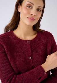 Cárdigan de punto color burdeos con cuello redondo, mangas largas y botones tipo perla en una tela suave y texturizada.