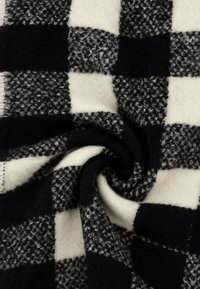 Coperta a scacchi bianca e nera con superficie morbida e testurizzata. Presenta quadrati alternati solidi e decorati di varie dimensioni.