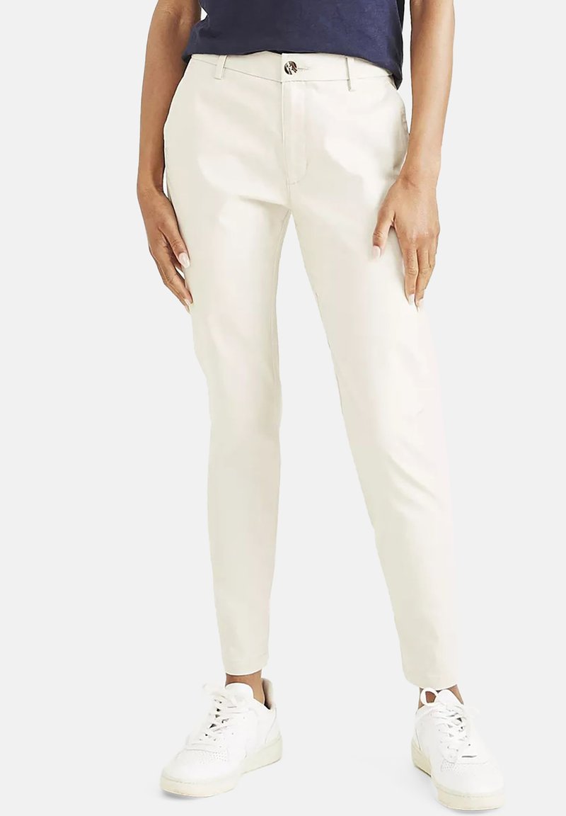 Béžové slim-fit nohavice vyrobené z hladkej tkaniny, s jemným leskom, prednými vreckami a zapínaním na gombík. Spárované s bielymi teniskami.
