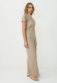 Beige geribbelde gebreide top met korte mouwen, gecombineerd met wijde broekspijpen. Glad textuur, subtiele glans en zijsplitten aan de onderkant.