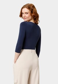 Námořnická modrá body s dlouhým rukávem a kulatým výstřihem, doplněná béžovými kalhotami s vysokým pasem a bočními kapsami. Hladká, přiléhavá tkanina.