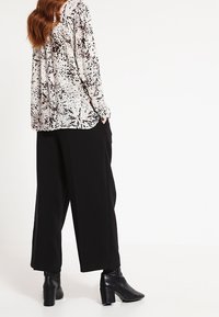 Camicia a maniche lunghe, dalla vestibilità ampia, in un motivo astratto nero e crema, abbinata a pantaloni neri a vita alta e gamba larga e stivaletti a punta.