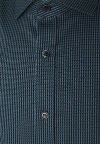 Katoenen shirt in donkerblauw met een gestructureerd ruitpatroon, voorzien van een puntkraag en twee zwarte knopen op de sluiting.