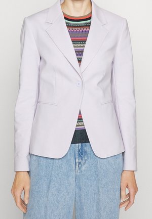 Femme portant un blazer lavande clair à un seul bouton sur un pull rayé coloré et un jean en denim bleu clair.